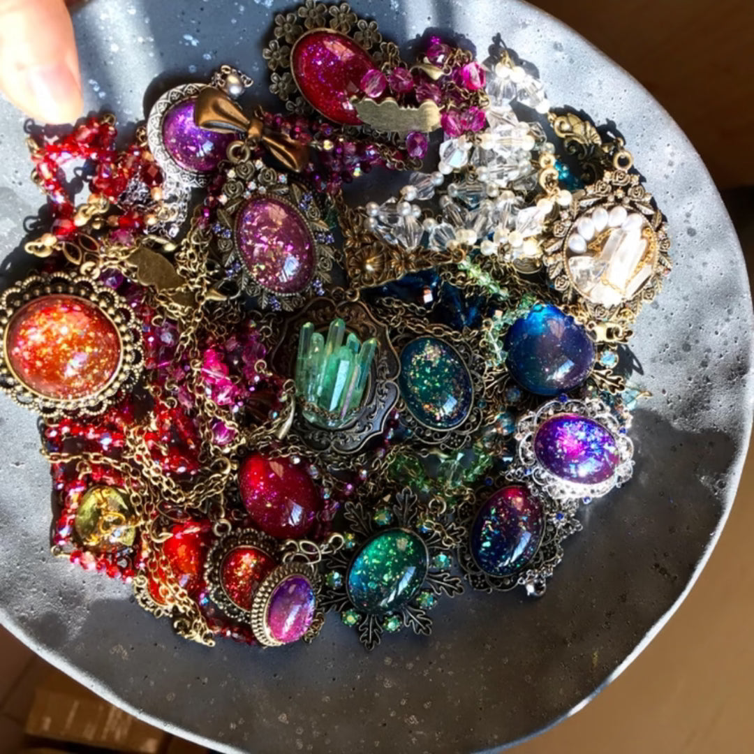 BrassBound Pages handmade resin gemstones and vintage metal charms in a sunlit tray, the colour-set used to build spellbound fantasy steampunk journal covers like Cassian Spectrum