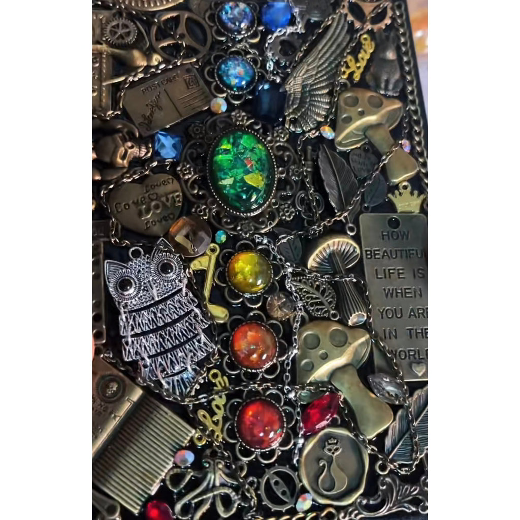 BrassBound Pages Cassian Spectrum close-up showing emerald centre stone, rainbow gems, owl charm, mushrooms and chained clockwork details