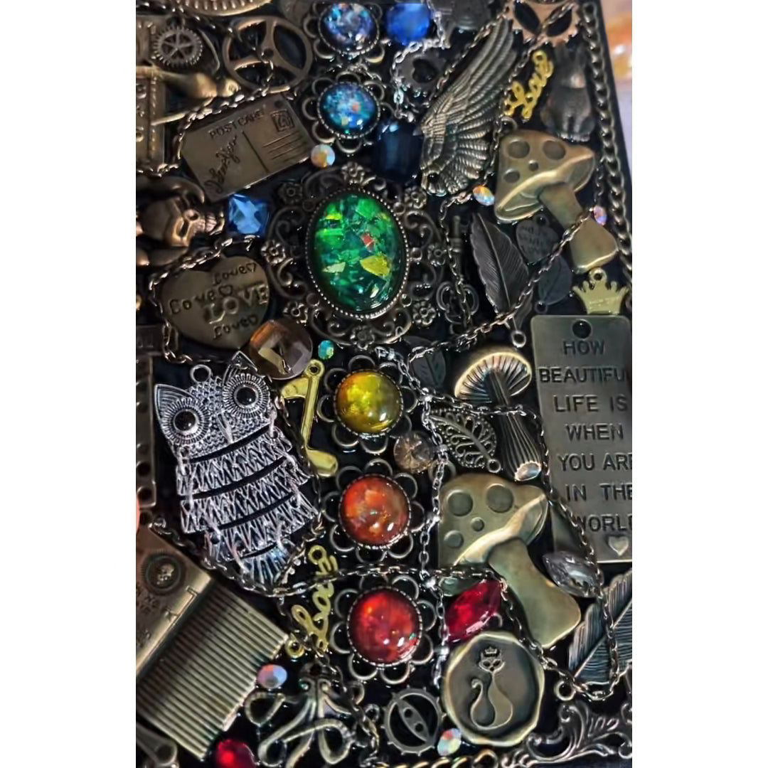 BrassBound Pages Cassian Spectrum close-up showing emerald centre stone, rainbow gems, owl charm, mushrooms and chained clockwork details