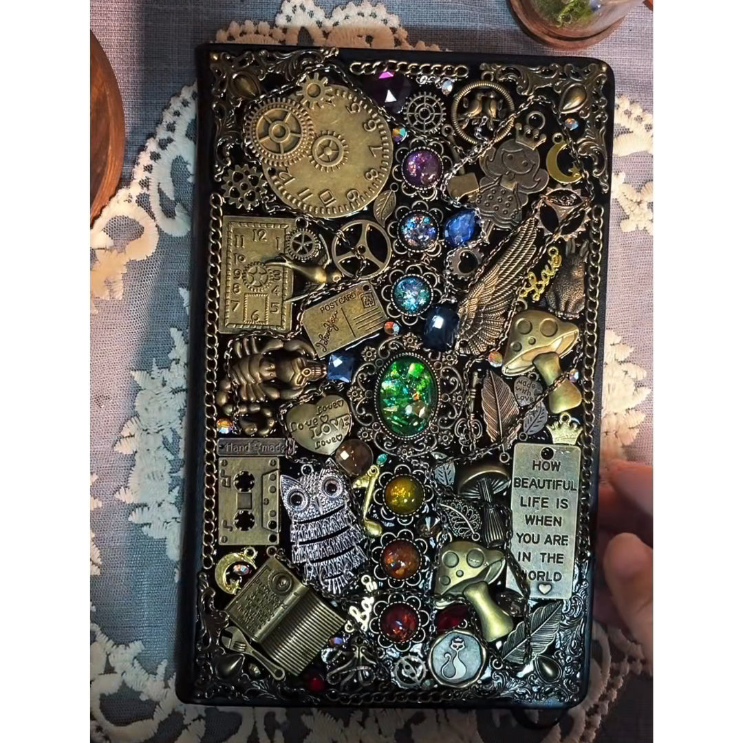 BrassBound Pages Cassian handmade fantasy steampunk journal with clock dial, emerald core and rainbow gem cabochons on an ornate black cover