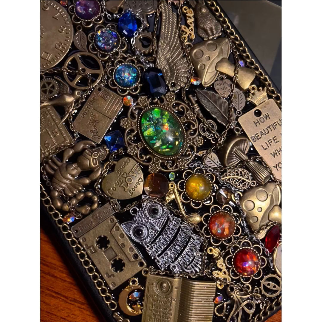 BrassBound Pages Cassian Spectrum angled detail of emerald core, blue and red gems, wing charm, gears and quote tag on steampunk journal cover